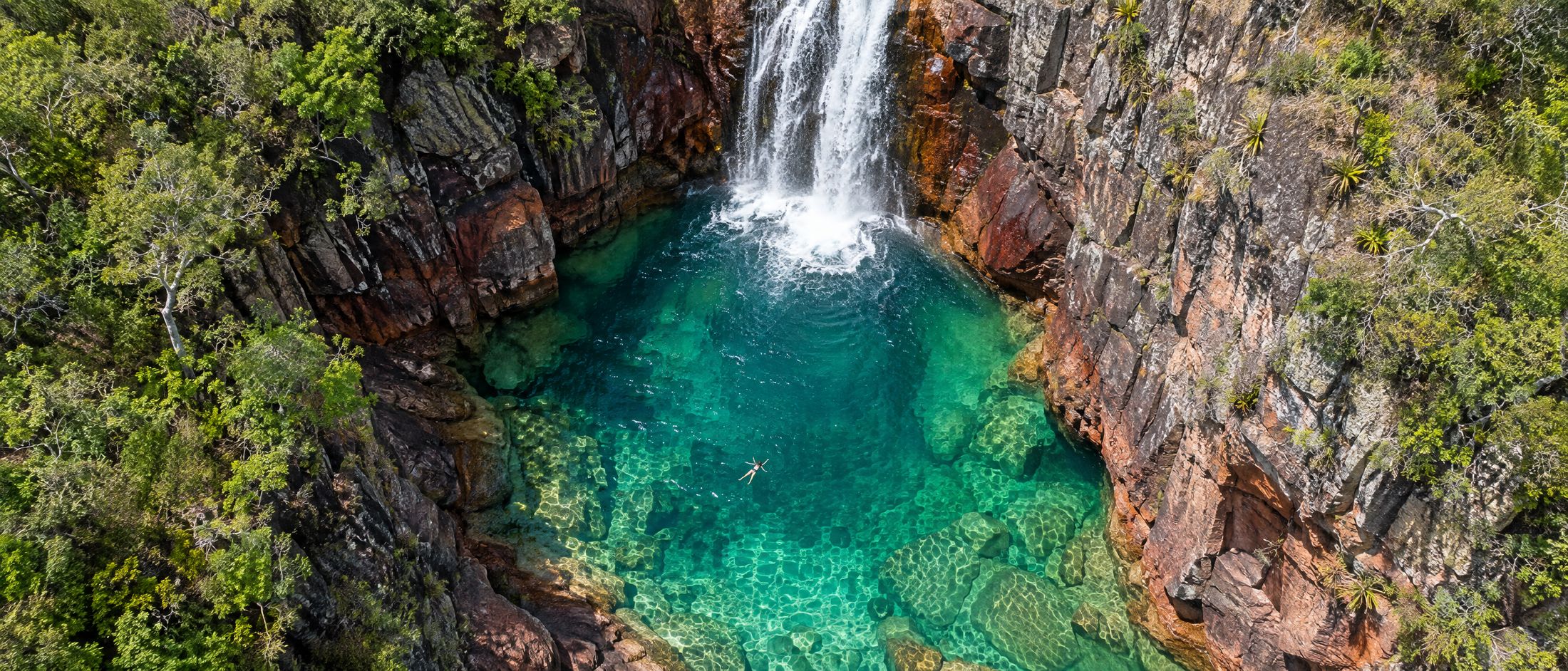 Vista aérea de uma cachoeira caindo num poço de água cristalina entre paredões de quartzito